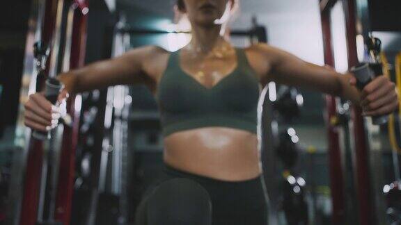 年轻的健身女性在健身房用交叉缆绳机锻炼手臂和肩部肌肉
