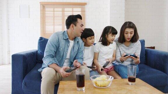 快乐的亚洲家庭爸爸妈妈和孩子们坐在客厅的沙发上玩着有趣的智能手机在线游戏