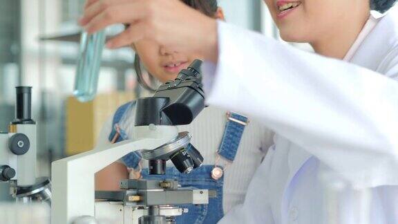 亚洲小孩和老师在学校实验室用显微镜观察小女孩用显微镜学习科学课教育的主题