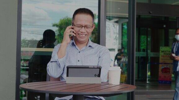 一名40-50岁的亚裔男子正在餐厅喝咖啡用4k视频在智能手机上阅读信件或短信休闲时间的热拿铁艺术咖啡