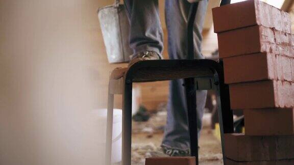 一名建筑工人正拿着一桶水泥溶液站在修理室的椅子上