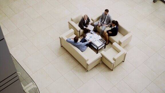 顶视图的一组商务人士同事讨论财务图表坐在沙发上的大厅在现代商业中心