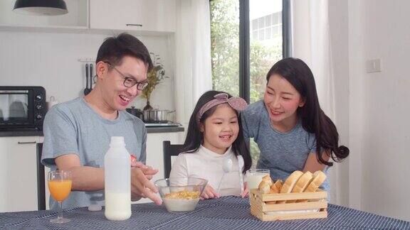 日本亚裔家庭在家里吃早餐亚洲的妈妈爸爸和女儿感觉愉快的谈话在一起吃面包玉米片谷物和牛奶在碗在厨房的桌子上在早上缓慢的运动