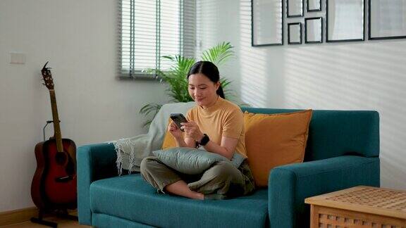 亚洲女性坐在家里客厅的沙发上用智能手机上网休息