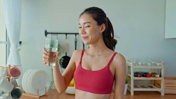 亚洲美女肖像在家里锻炼后喝水年轻美丽口渴的运动女孩在家里的厨房为保健锻炼后喝一杯干净的天然矿物质