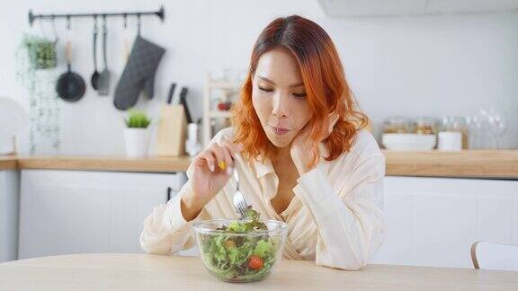 亚洲有吸引力的女人在家里厨房的桌子上吃绿色沙拉年轻美丽的素食女孩感到快乐享受早餐蔬菜健康的食物在家里减肥健康