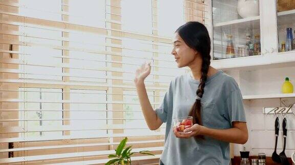 年轻的亚洲女人在家里的厨房里吃着幸福的草莓人们健康的生活方式