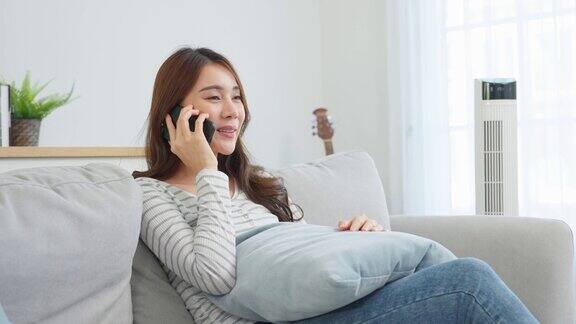 亚洲美女坐在沙发上在家里打电话快乐迷人的年轻女孩在家里度过休闲时光放松心情享受在客厅用智能手机交流和讨论