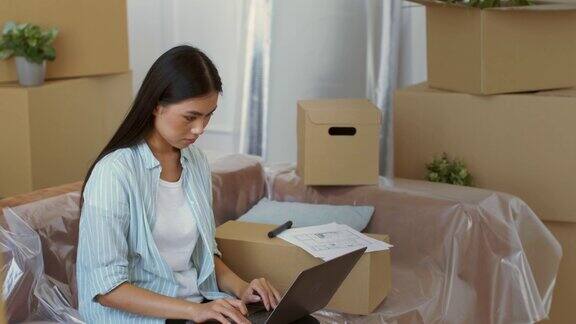 亚洲女性在室内移动箱子之间用笔记本电脑工作