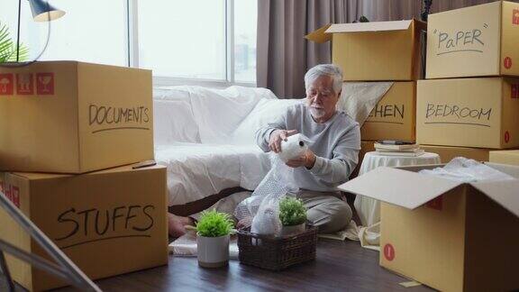水平中拍摄的成年年长的亚洲男子男子白胡子坐在地板上准备搬到新房子包装东西到盒子和胶带他们在客厅家庭搬家的想法概念