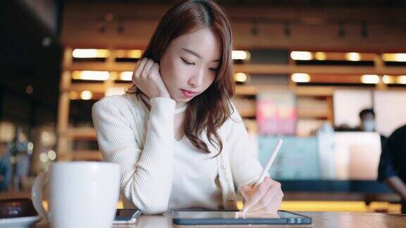 年轻的成年人快乐微笑的亚洲学生在线学习在网上聊天在网上聊天会议使用平板电脑在咖啡馆或办公室大学学院女生远程学习