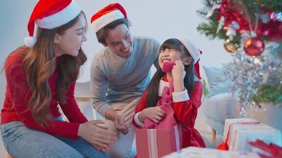 亚洲可爱的小女儿打开父母送来的礼物盒幸福的家庭小屁孩感到幸福和兴奋的惊喜来自妈妈和爸爸准备在家里一起庆祝圣诞节