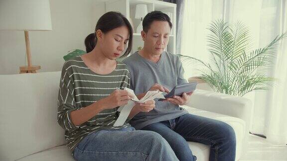 亚洲夫妇用计算器计算水电费计算支票信用卡收据每月开支账单一起坐在家里客厅的沙发上生活方式花时间在家里