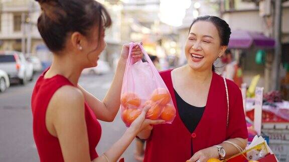 4K亚洲母亲和女儿在唐人街购买庆祝中国农历新年的新鲜水果