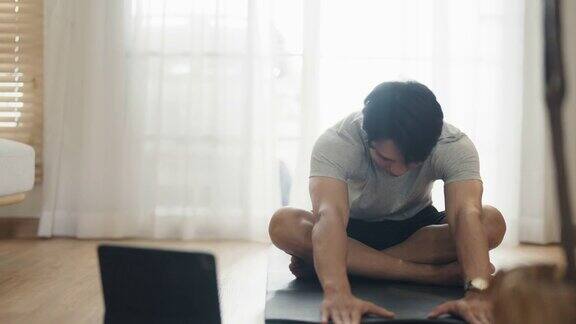年轻人在公寓垫子上用笔记本电脑练瑜伽