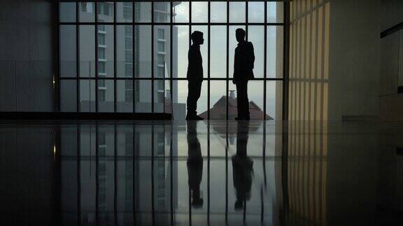 两名商人站在大全景窗旁的剪影在一间有大窗户的大办公室里