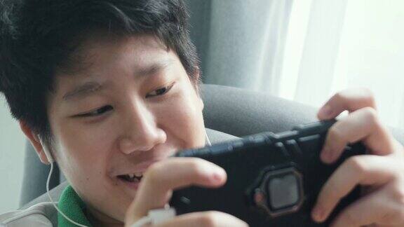 亚洲男孩躺在家靠窗的沙发上玩手机游戏生活理念