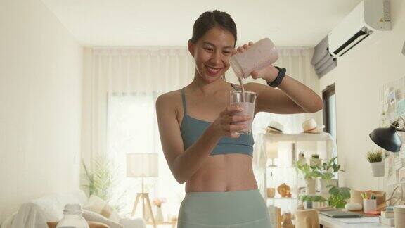 年轻的亚洲运动员女子使用搅拌机和倾倒冰沙在家里的玻璃健康食品
