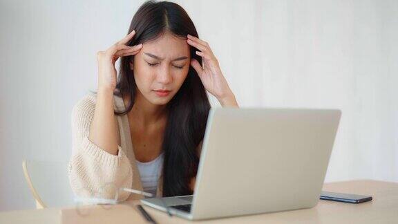 办公室综合症劳累过度的年轻亚洲妇女感觉头痛电脑笔记本电脑工作后视力问题压力大的年轻女性在家里饱受疲劳之苦