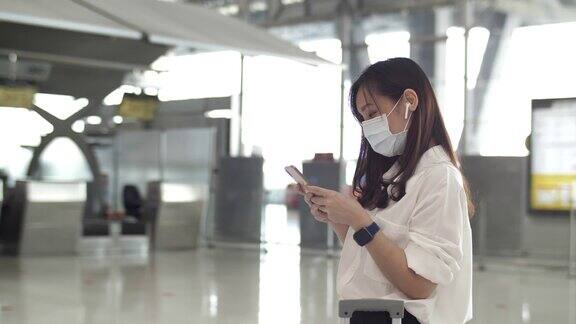 亚洲女性在机场使用智能手机时戴上防护口罩