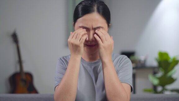 一名亚洲妇女坐在家里的沙发上眼睛疼得难受