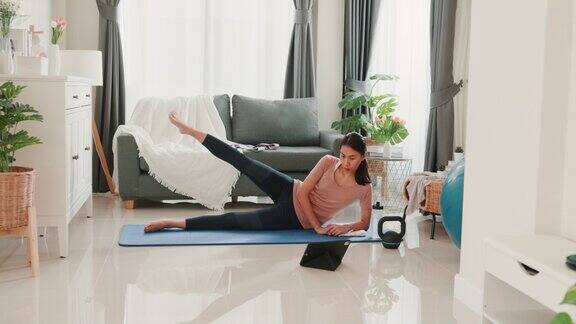 年轻迷人的亚洲女性在运动服观看健身在线视频平板电脑练习瑜伽初学者在客厅在房子