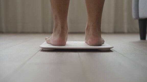 年轻女子在家里锻炼后在体重秤上测量体重