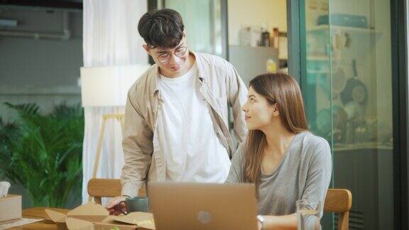 年轻的亚洲夫妇聊天吃零食一起在家里工作