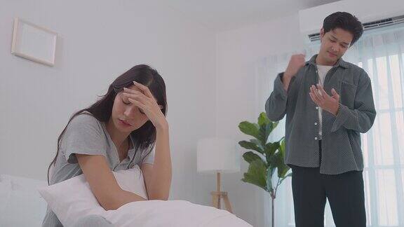亚洲年轻夫妇坐在床上痛苦的争吵后打架新婚男女因在卧室里吵架而伤心欲绝紧张的亚洲女人坐在床上哭
