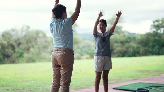 亚洲华人女子在高尔夫练习场与教练进行热身运动
