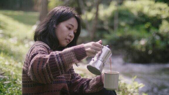 在瀑布附近的森林里一名年轻女子正在往杯子里倒咖啡