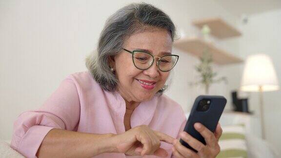 老妇人坐在家里的沙发上玩智能手机