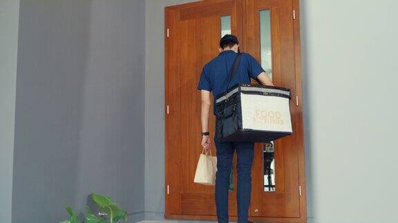 年轻的亚洲快递员戴着面具穿着蓝色海军制服携带箱子箱子敲门送货上门网上购物纸袋到客户家门口