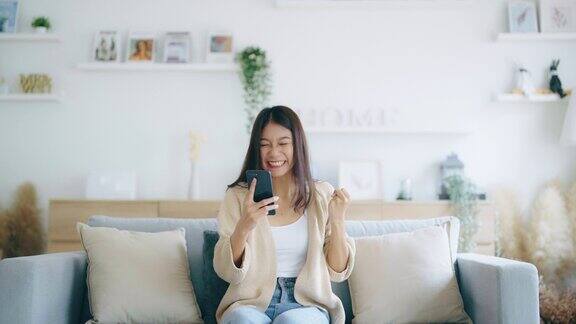快乐的年轻亚洲女人放松在家里舒适的沙发上发短信在智能手机上微笑的女孩使用手机聊天在线消息从家里网上购物