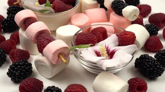 小碗里放着锦葵树、覆盆子、黑莓和蓝莓的花在白色的桌子上放着浆果串和棉花糖野餐和聚会