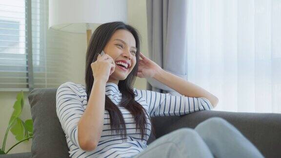 亚洲美女坐在家里的沙发上用手机聊天快乐迷人的年轻女孩在家里度过休闲时间感到放松享受在客厅用智能手机交流和讨论