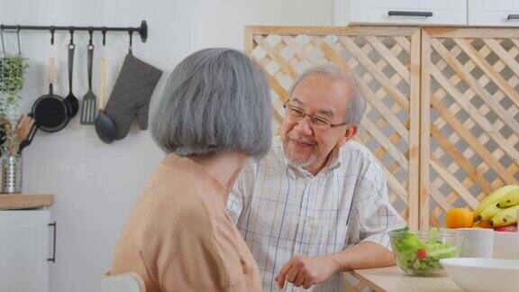 亚洲老年夫妇在家里的厨房里一起吃沙拉幸福的家庭有魅力的年长成熟的夫妻坐在餐桌上享受退休生活午餐吃健康的食物在家里