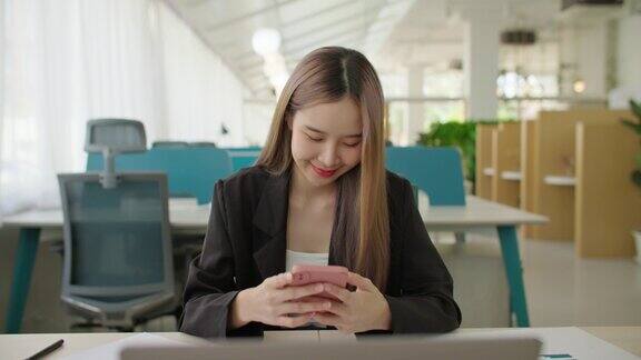 年轻快乐的亚洲商业女性自由使用智能手机在现代办公室