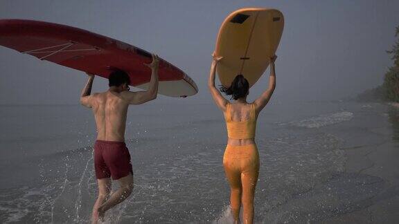 带着冲浪板冲进海浪的快乐夫妇