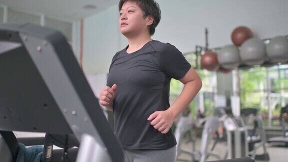 成熟的亚洲华人女子在健身房跑步机上跑步