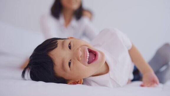 亚洲父母和年幼的儿子在家里的卧室里度过闲暇时光迷人的夫妇和小男孩感到快乐和放松享受一起在床上玩耍家庭-父母关系概念