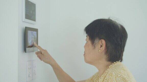亚洲老年妇女通过家中的智能设备打开前门老年妇女使用科技