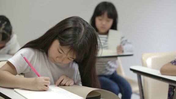 亚洲小女孩在笔记本上写字在教室里考试