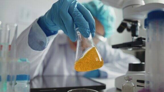 科学家戴着手套手持装有黄色液体的无菌烧瓶油品研究与有毒液体概念