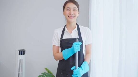 亚洲清洁服务女工在客厅工作的肖像美丽的女孩家庭主妇管家清洁工感到高兴擦窗户为家务或家务然后看着相机
