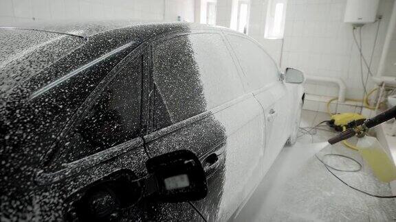 在车库里工人正在用肥皂泡沫覆盖车身进行清洗用软管进行喷涂洗车