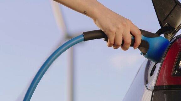 SLOMO手动拔出电动汽车插头从一辆由风力涡轮机提供绿色能源的汽车