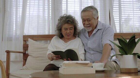 一对亚洲老夫妇坐在客厅里看书面带微笑地坐着聊天