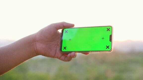 手持绿色屏幕和自然背景的智能手机色度键