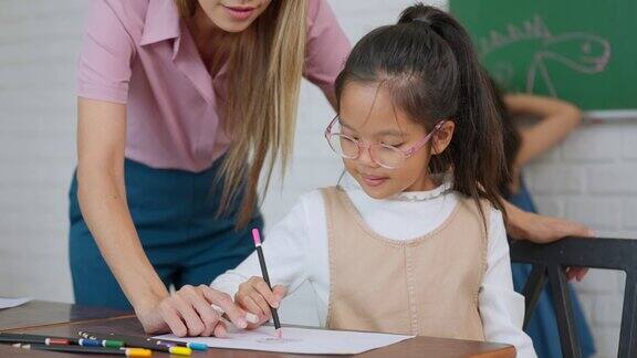 年轻的女小学老师在教室里帮助一个小女孩白人女教师在帮助小女孩写作教育与学习理念